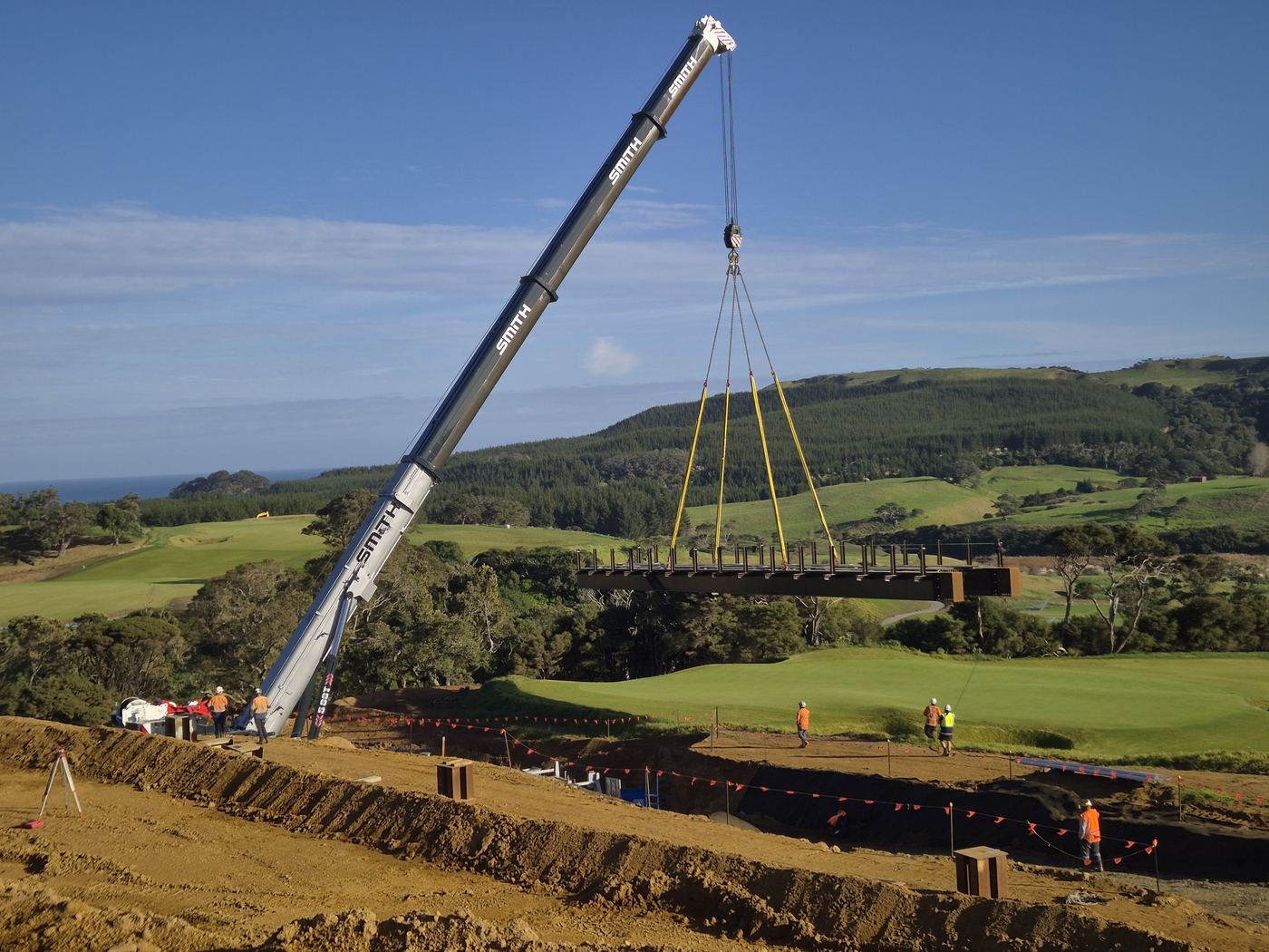 Crane lifting a bridge into place over a creek on a coastal course